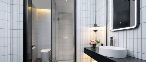 A modern bathroom with a glass-enclosed shower, a white toilet, a black countertop, a white sink, and a mirror.