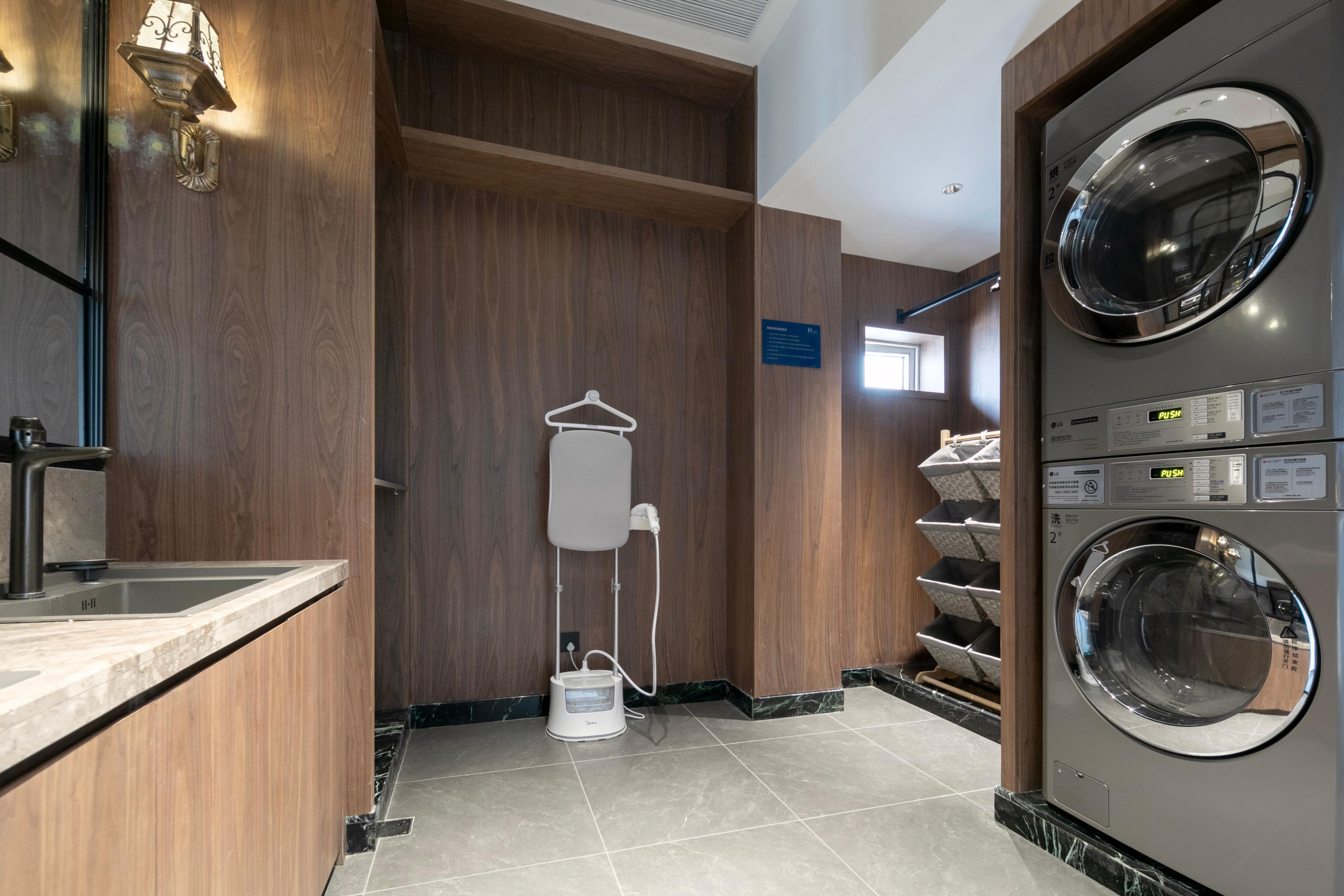 Een hotelbadkamer met een wastafel, een spiegel, een handdoekhouder, een douche en een wasmachine.