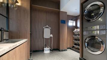 Een hotelbadkamer met een wastafel, een spiegel, een handdoekhouder, een douche en een wasmachine.