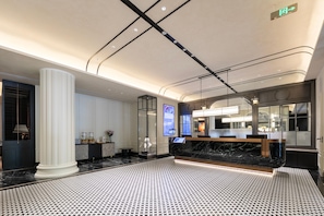 Um saguão de hotel com balcão de recepção, uma coluna grande e piso estampado.