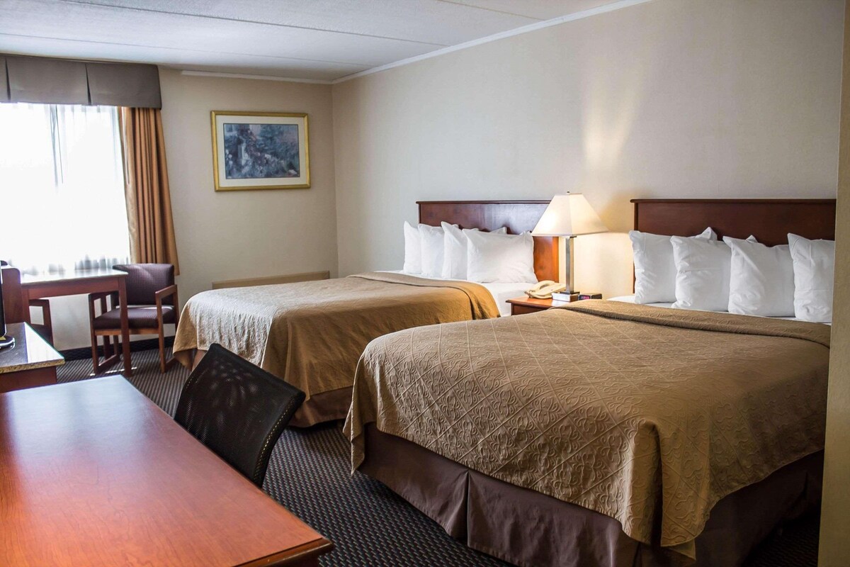Una habitación de hotel con dos camas, un escritorio, una silla y una lámpara.