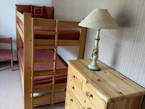 Ein Stockbett mit einer Stehle, eine Holzkommode mit Schubladen und eine Tischlampe.