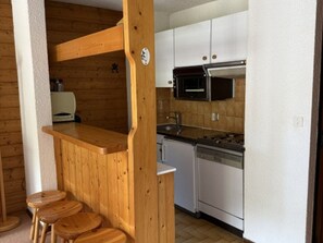 Eine kompakte Küche mit Holzelementen, einer Mikrowelle, einem Herd und einer kleinen Bar mit Hockern.