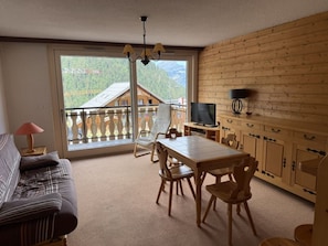 Ett mysigt rum med en soffa, ett matbord med stolar, en tv och träskåp.