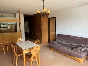 Ett matbord i trä med stolar, en soffa och en köksdel med en hängande lampa.