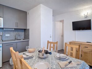 A compact kitchen with modern appliances, a dining table set for four, and a flat-screen TV mounted on the wall. - Apartment at the foot of the slopes - 4 guests (Les Menuires)