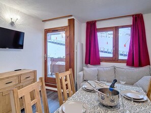 A room with a dining table set for two, a television mounted on the wall, and a window with curtains. - Apartment at the foot of the slopes - 4 guests (Les Menuires)