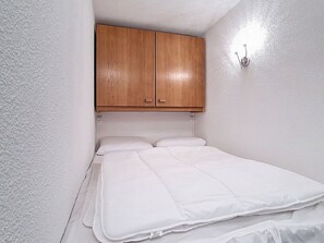 A small, single-bed room with a wooden wardrobe above the bed and a wall-mounted light fixture. - Apartment at the foot of the slopes - 4 guests (Les Menuires)