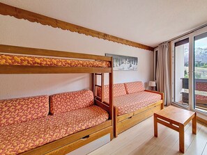 A room with a bunk bed, a sofa, a small table, and a window with a view of mountains. - Bright studio at the slopes - 3 guests (Les Menuires)
