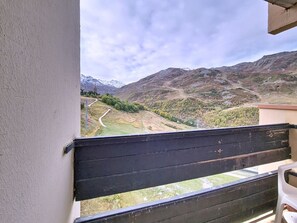 A balcony with a view of a mountainous landscape, a winding road, and a distant building. - Bright studio at the slopes - 3 guests (Les Menuires)
