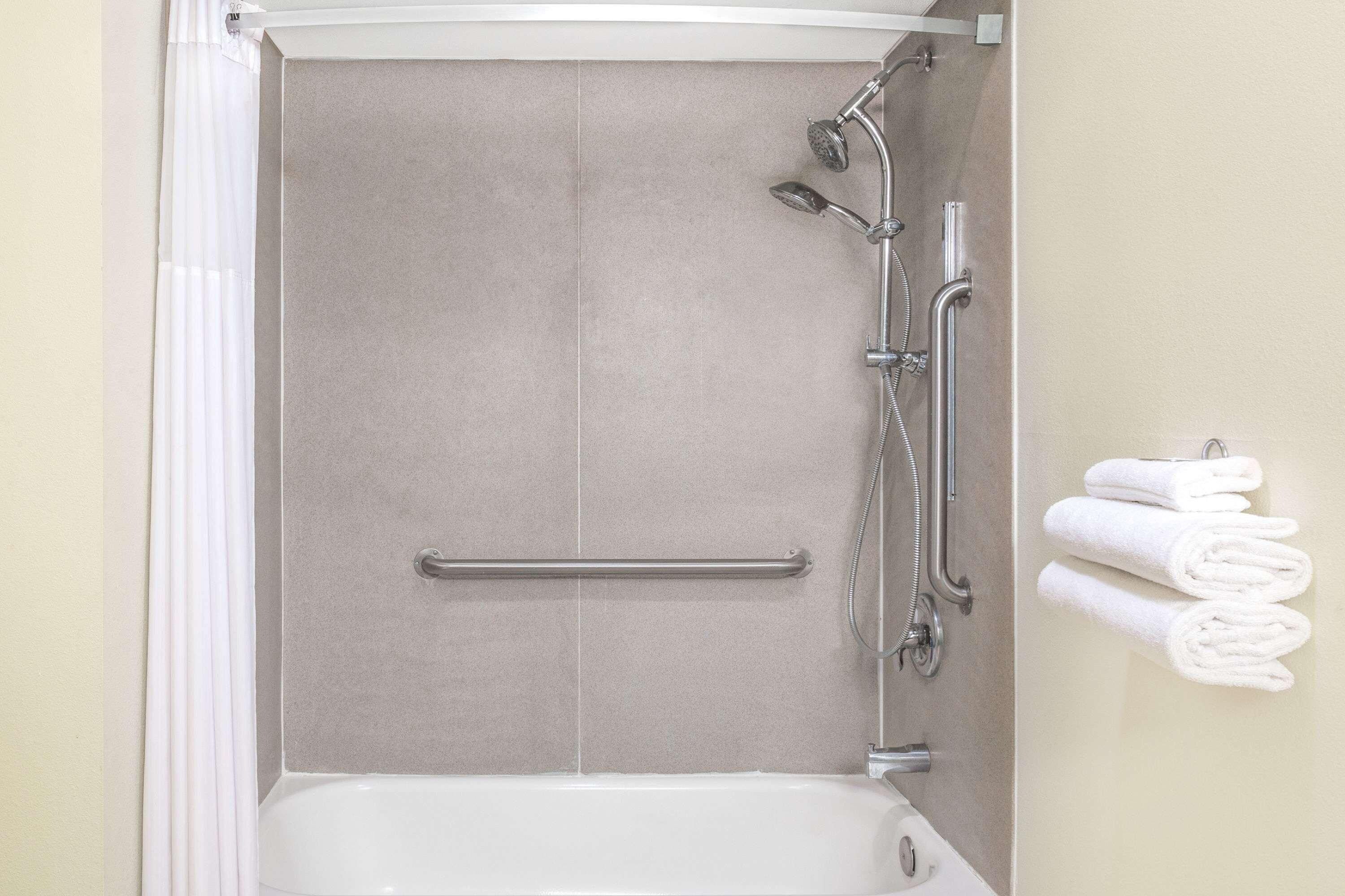 A shower enclosure with a grab bar, a handheld showerhead, and a handheld showerhead with a hose.