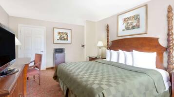 A hotel room with a bed, a desk with a television, a chair, a nightstand with a lamp, and two framed pictures on the wall.