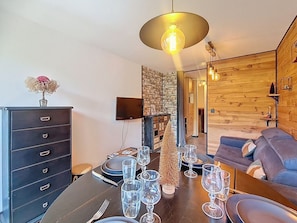 A dining area with a table set for a meal, a sofa, and a TV mounted on the wall. - Bright apartment, balcony - 4 guests (Les Menuires)