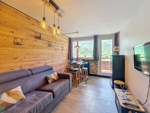 Un accogliente soggiorno con parete in legno, un divano, un tavolo da pranzo e una TV.