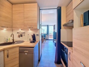 A compact kitchen with wooden cabinets, a built-in dishwasher, and a coffee machine. - Bright apartment, balcony - 4 guests (Les Menuires)
