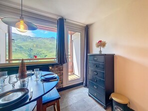 Un'area pranzo con un tavolo apparecchiato per due, vista su un paesaggio verde dalla finestra e un mobile scuro con cassetti.