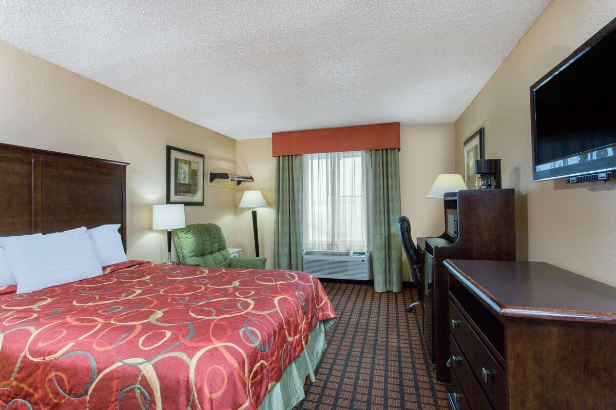 A hotel room with a bed, a desk, a chair, a television, and a window with curtains.