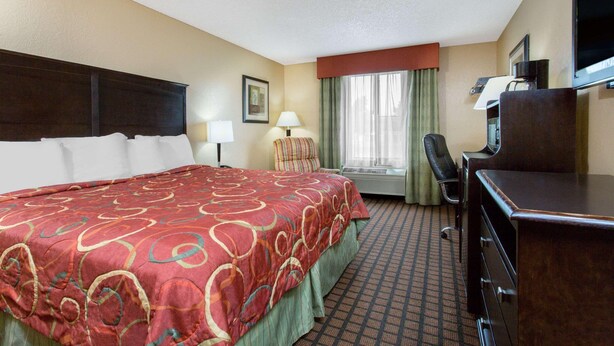 A hotel room with a large bed, a desk, a chair, a television, and a window with curtains. - Texarkana Inn (Texarkana)