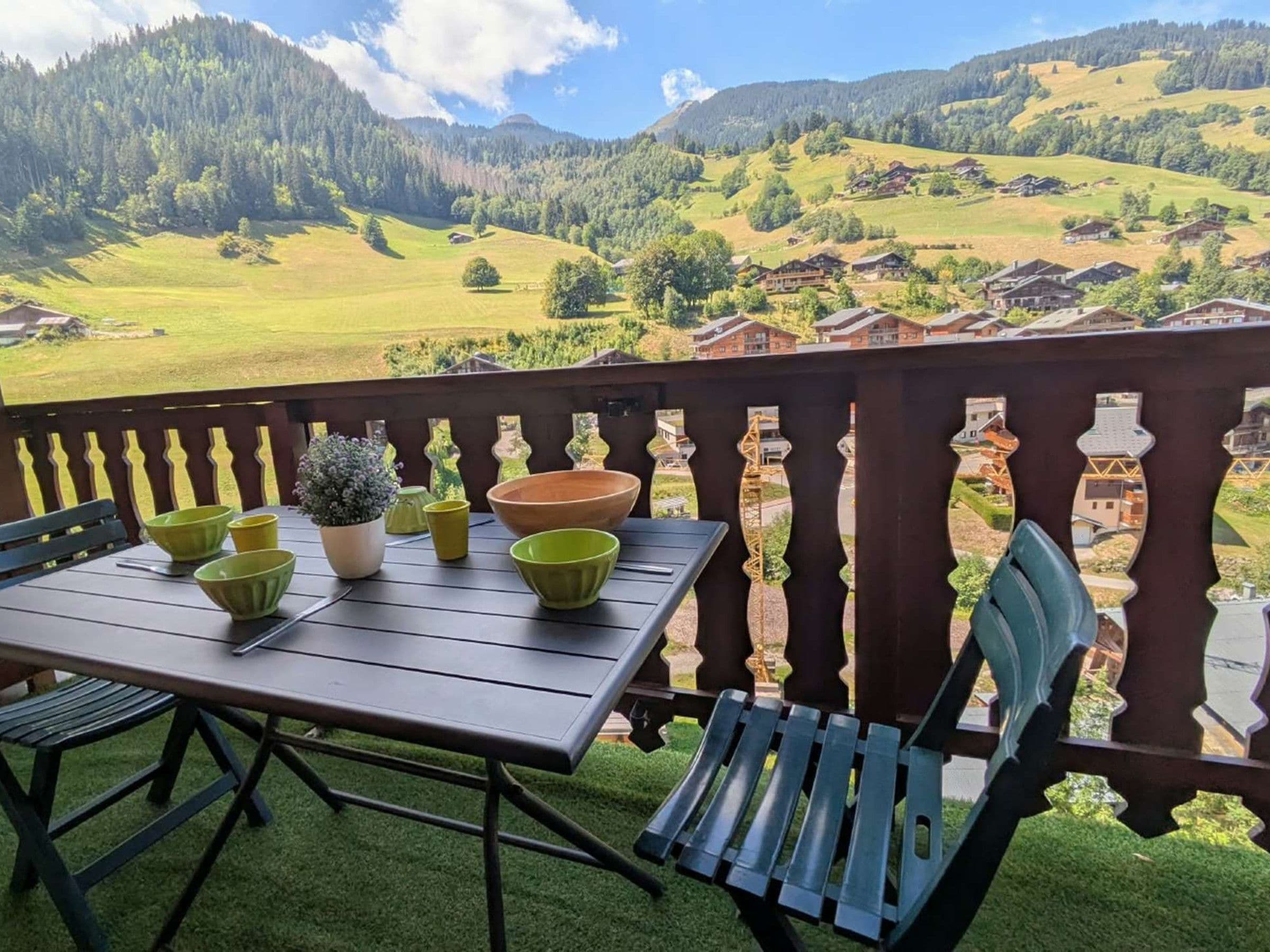 A balcony with a table and chairs, overlooking a mountainous landscape with houses.
