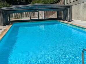 Ein rechteckiger Swimmingpool mit klarem, blauen Wasser, umgeben von einer Betonplattform und einem Metallzaun.
