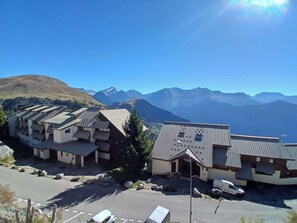 A hotel with multiple buildings, a parking area, and a mountainous backdrop. - 2-room apartment - 5 guests, south balcony, L'Alpe d'Huez (Huez)