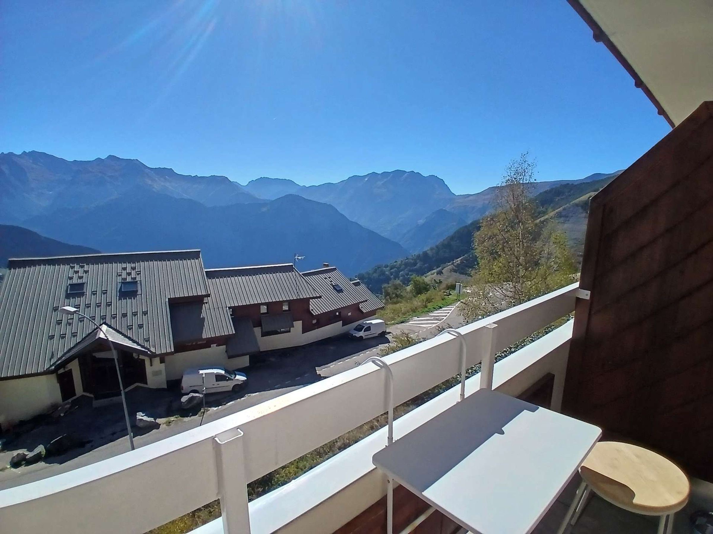 A balcony with a view of a mountain range, a building with a sloped roof, and a white table and chair.