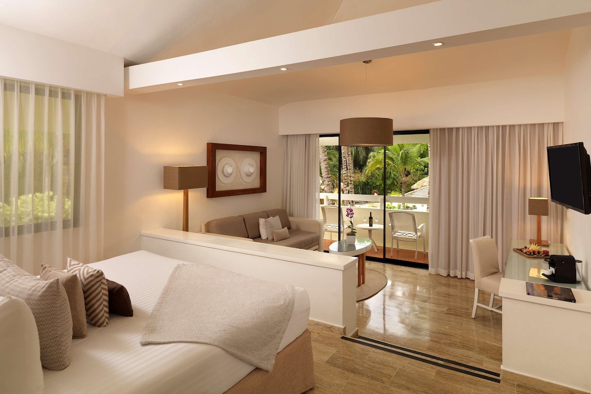 A hotel room with a bed, a sitting area with a table and chairs, a TV, and a view of the outdoors.