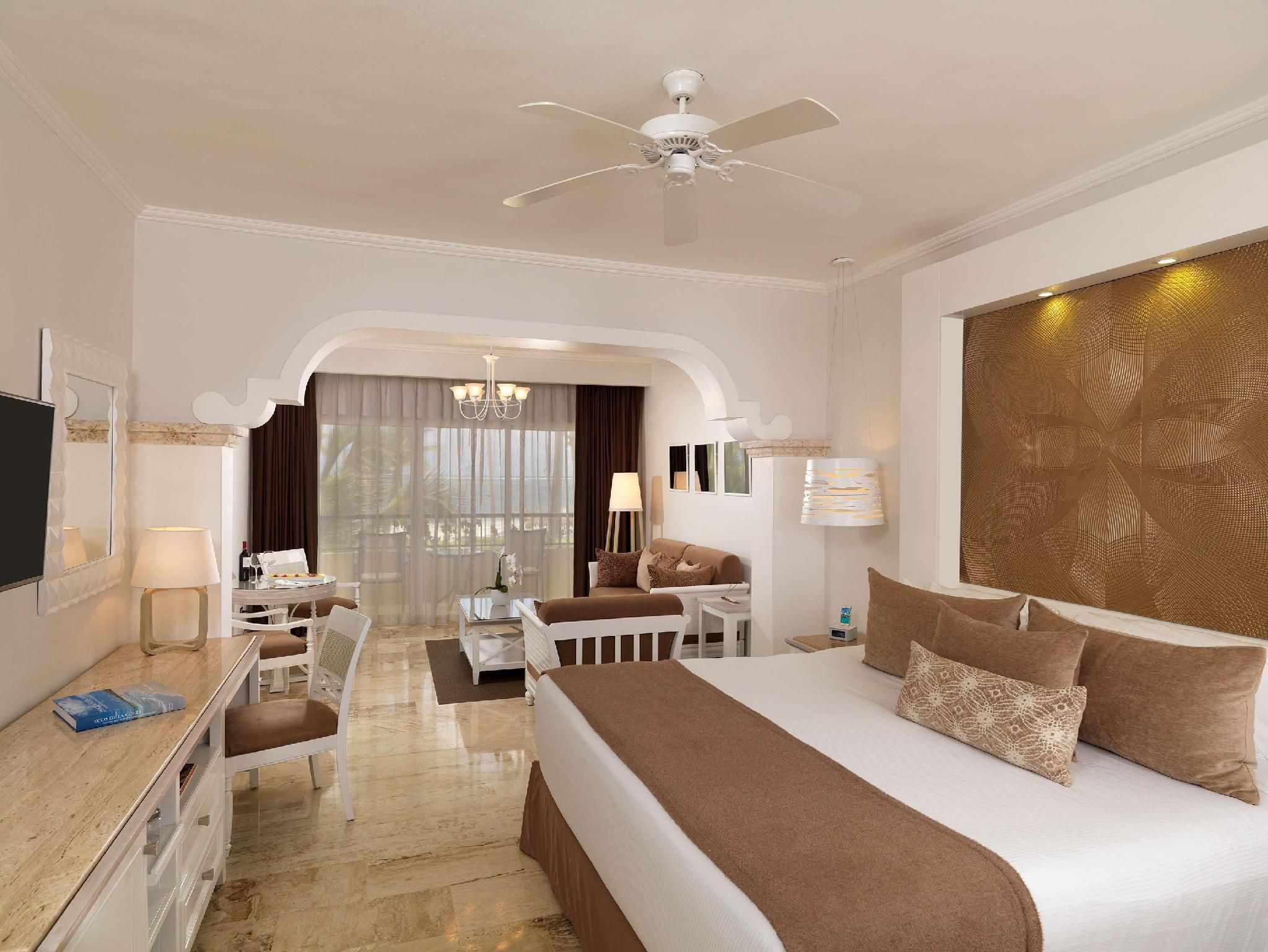 Habitación de hotel con cama, escritorio, silla, televisor y ventilador de techo.