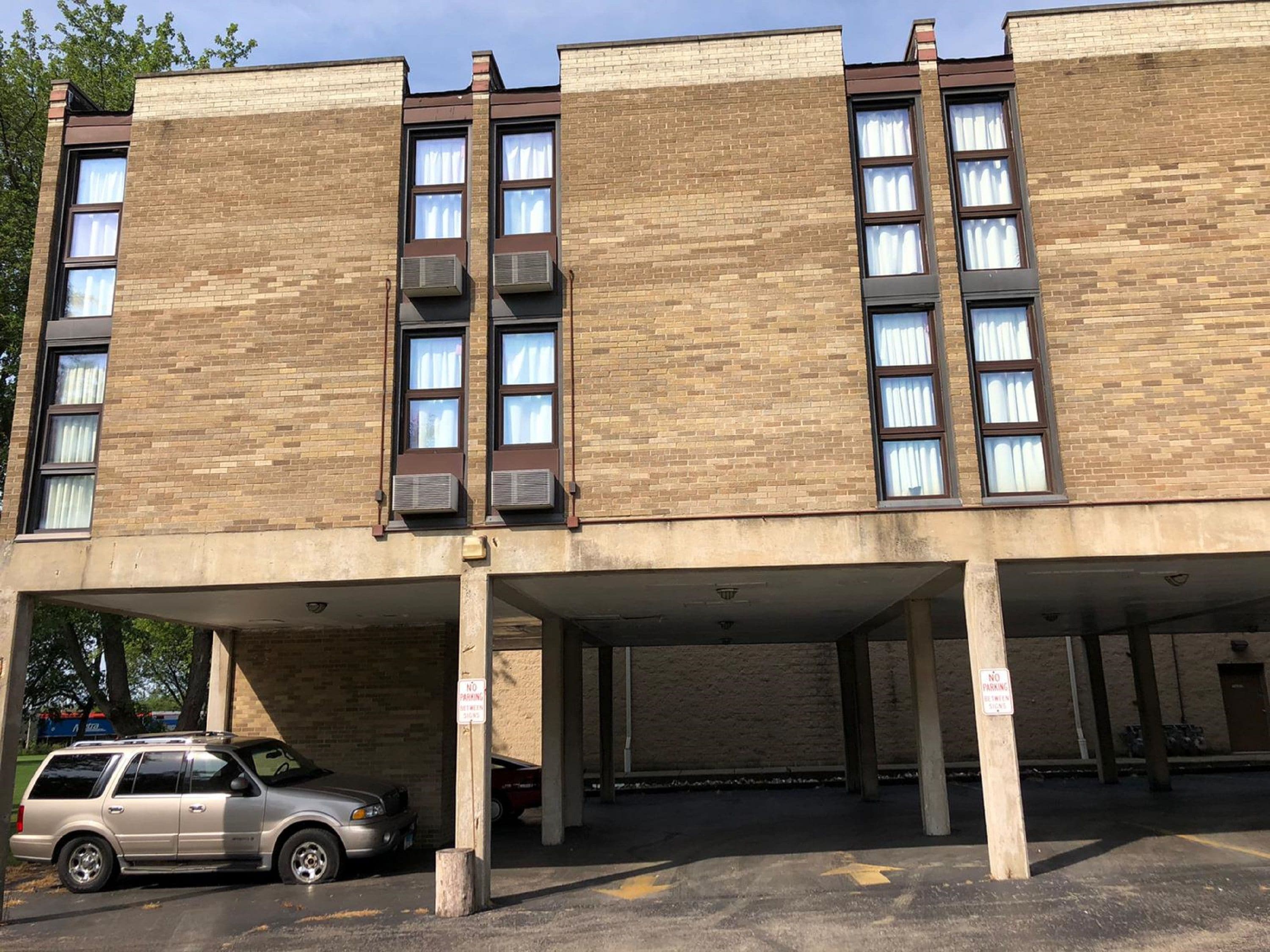 A multi-story parking garage with a beige brick facade, air conditioning units, and a parked SUV.