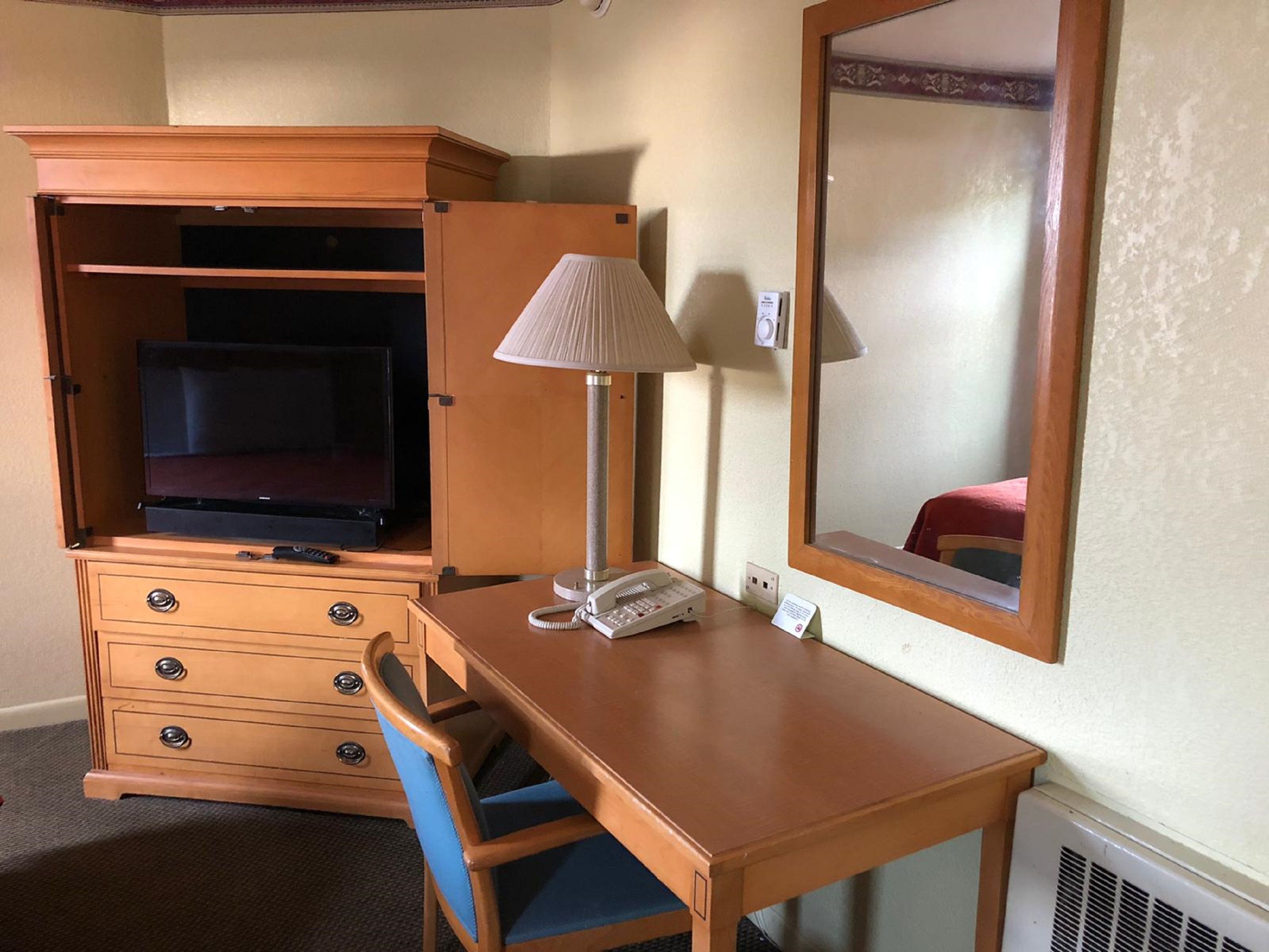 Camera d'albergo con una scrivania in legno, un telefono, una lampada, uno specchio, una TV in un mobile e una sedia.