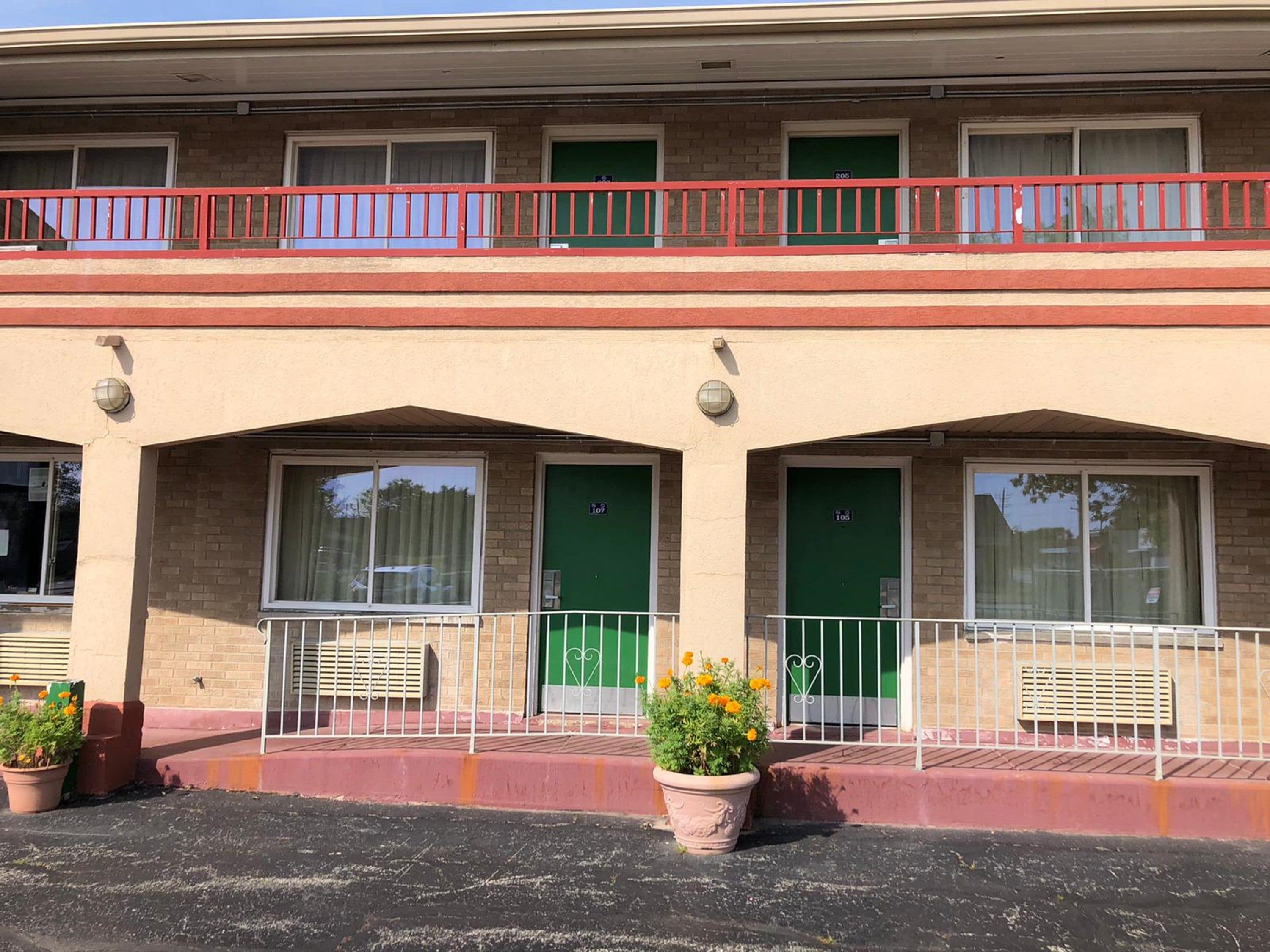 Un edificio a due piani con ringhiera del balcone rossa, porte verdi e piante in vaso al piano terra.