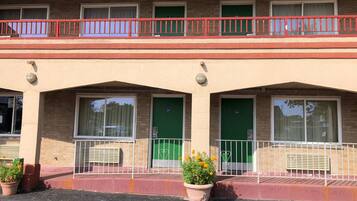 Un edificio a due piani con ringhiera del balcone rossa, porte verdi e piante in vaso al piano terra.
