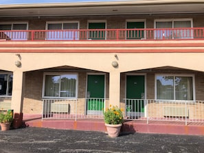Un bâtiment à deux étages, doté d’un balcon avec une rambarde rouge, de portes vertes et de plantes en pot au rez-de-chaussée.