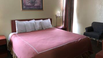 Camera d'albergo con un letto grande, una poltrona, un comodino, una lampada e un quadro appeso al muro.
