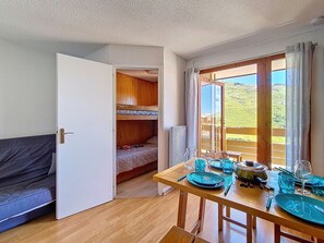 A room with a bunk bed, a dining table set for two, and a view of a green landscape through a window. - Comfortable apartment - 4 guests. At the slopes (Les Menuires)