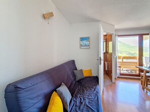 Um quarto com um sofá escuro, uma porta de madeira que dá para uma área externa e um cartaz na parede.