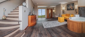 Un interior moderno con una escalera de madera, un armario de madera, un otoman amarillo, un ventanal grande y un jacuzzi.