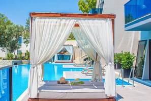 Zona de piscina amb una tenda, gandules i una taula petita amb una beguda i un barret.