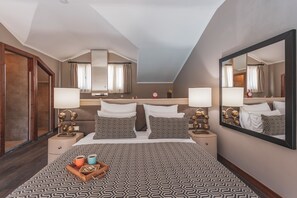 Habitació d'hotel amb un llit gran, dues taules de nit, un taulell, un mirall i una finestra amb cortines.