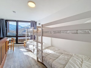 Ein Zimmer mit Etagenbetten, einem Schreibtisch und einem Stuhl, mit Blick auf Berge durch ein großes Fenster.