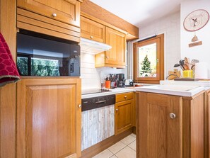 A kitchen with wooden cabinets, a Bosch dishwasher, a coffee maker, and a window with a view of a tree. - Bright apartment at the foot of the slopes - 4 guests (Les Menuires)