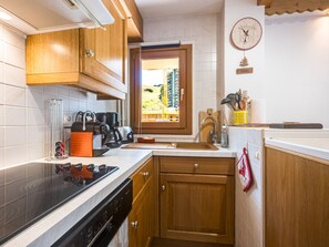 A kitchen with wooden cabinets, a stove, a coffee maker, and a window with a view of buildings outside. - Bright apartment at the foot of the slopes - 4 guests (Les Menuires)