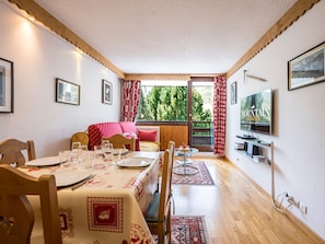 A dining area with a table set for four, a sofa, and a television on the wall. - Bright apartment at the foot of the slopes - 4 guests (Les Menuires)