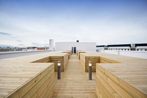 Una terraza de madera con zonas de estar y una entrada central que conduce a un edificio.