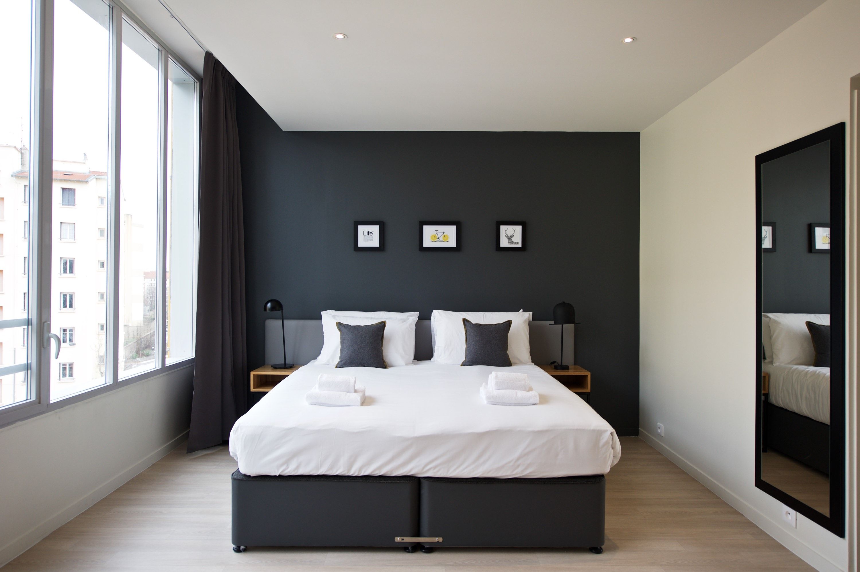 Une chambre d’hôtel moderne avec un grand lit, des murs sombres et une vue sur la ville.