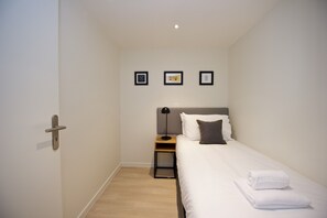 Una habitación pequeña y limpia con una cama individual, una mesita de noche, una lámpara y tres cuadros en la pared.