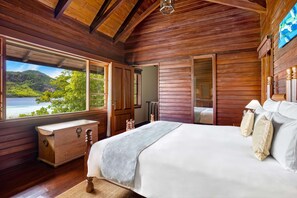 A wooden bedroom with a large bed, a wooden chest of drawers, and a view of a lake and mountains. - JA Enchanted Island Resort (Round Island)