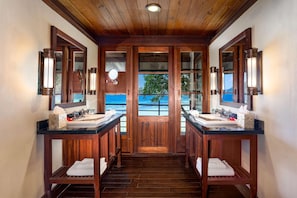 A hotel bathroom with two sinks, wooden flooring, and a view of the sea through large windows. - JA Enchanted Island Resort (Round Island)