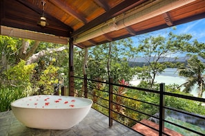 A large bathtub with red flowers on a balcony with a view of a tropical landscape and ocean. - JA Enchanted Island Resort (Round Island)