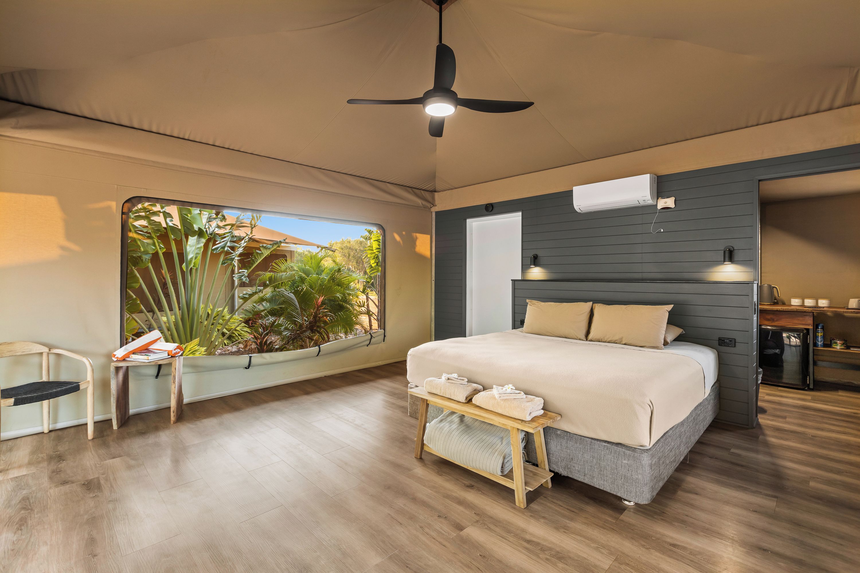 Une chambre moderne avec un lit, un ventilateur de plafond, une fenêtre donnant sur un paysage verdoyant et une petite table avec des serviettes.